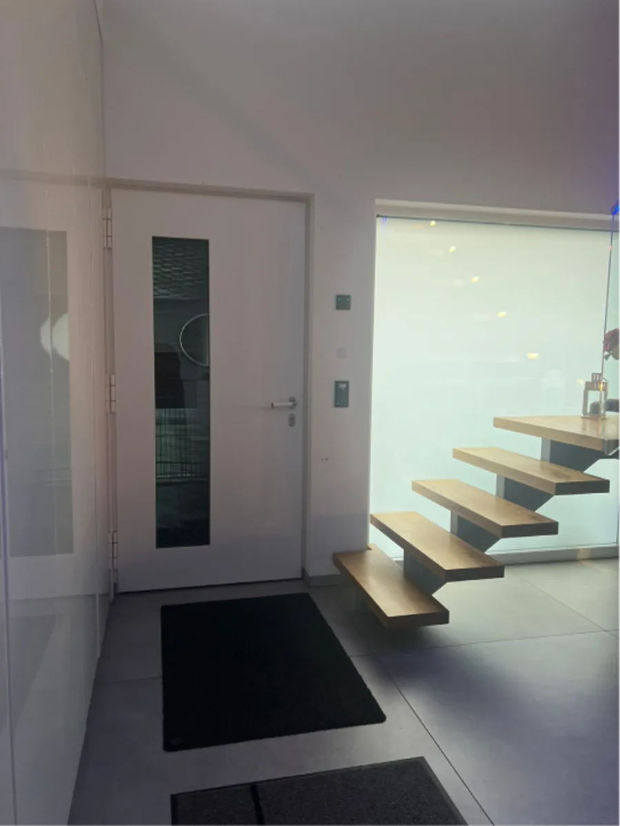 Eine moderne Eingangstür neben einer schwebenden Holztreppe.